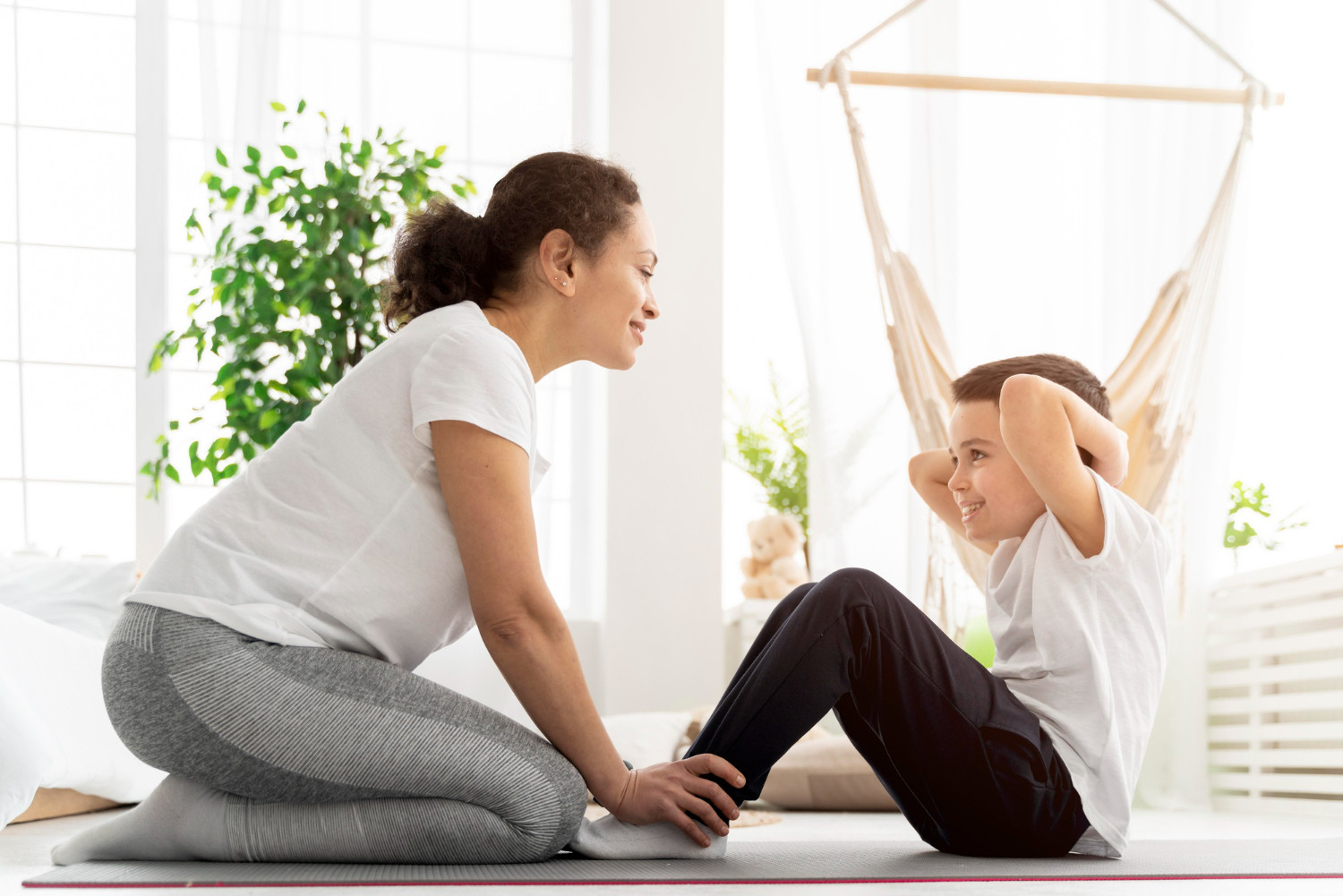 Physical therapist guiding a young boy through sit-ups on a mat