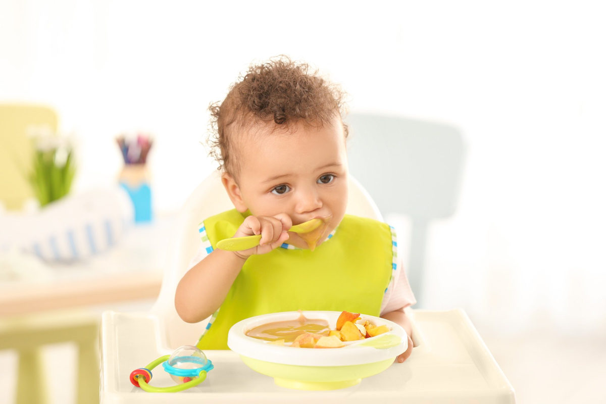 Toddler in a high chair feeding himself with a spoon