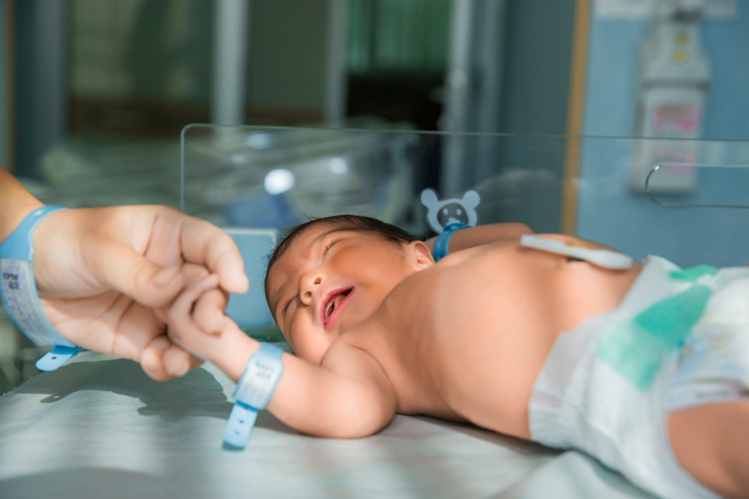 Parent holding the hand of a smiling newborn in a hospital bassinet