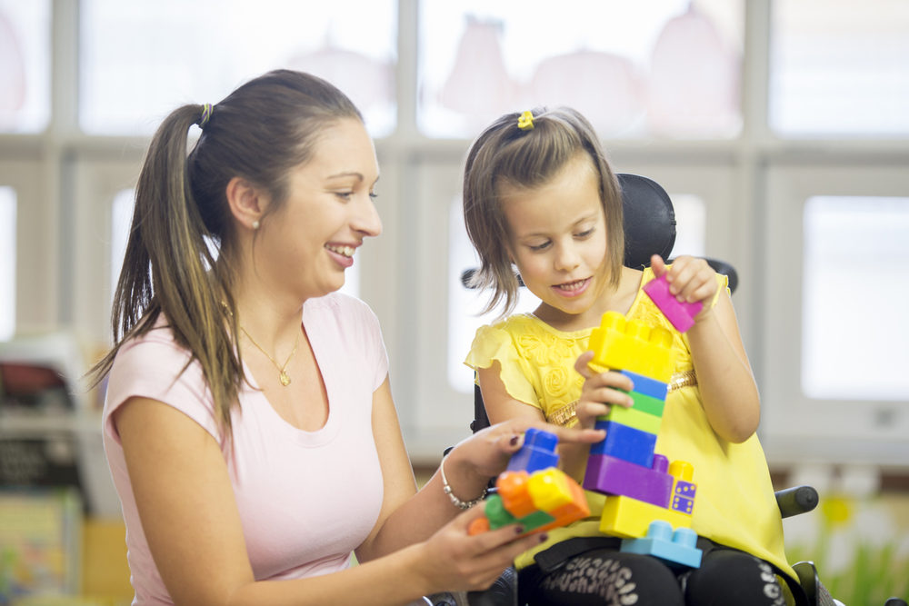 Adult building with blocks alongside a young girl in a wheelchair