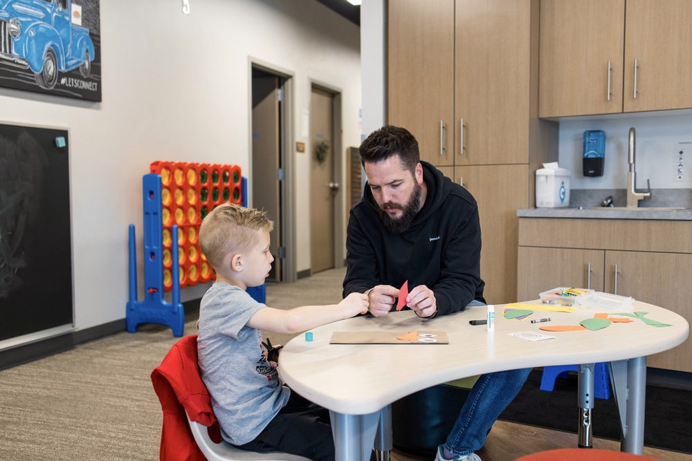 Adult and young boy doing a paper cutting activity at a table