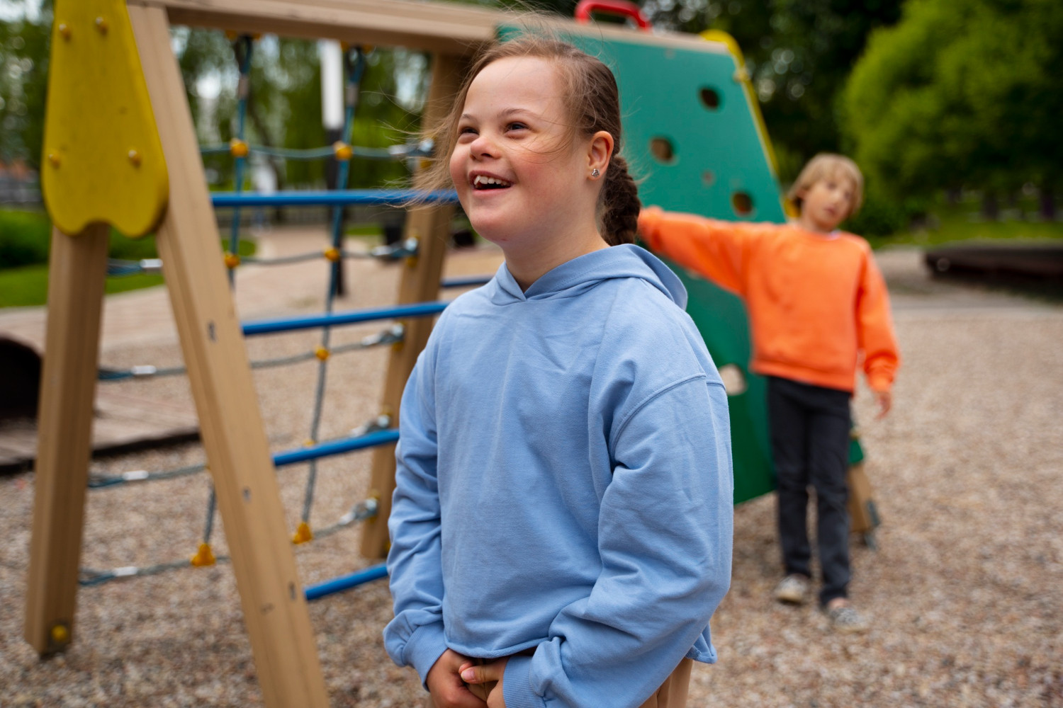 Smiling girl with Down syndrome in a blue hoodie at a playground