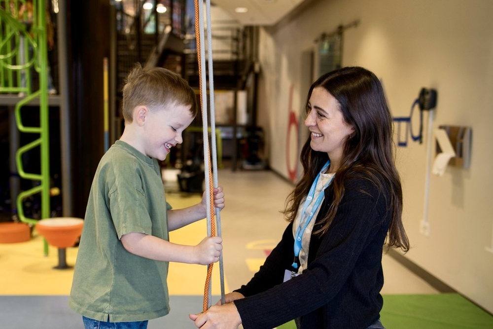Boy holding rope in a gym setting as a nearby adult smiles