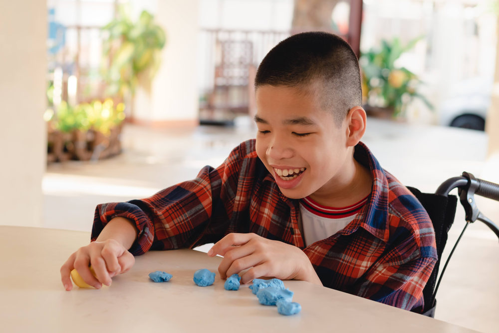 Smiling boy in a wheelchair playing with blue modeling clay